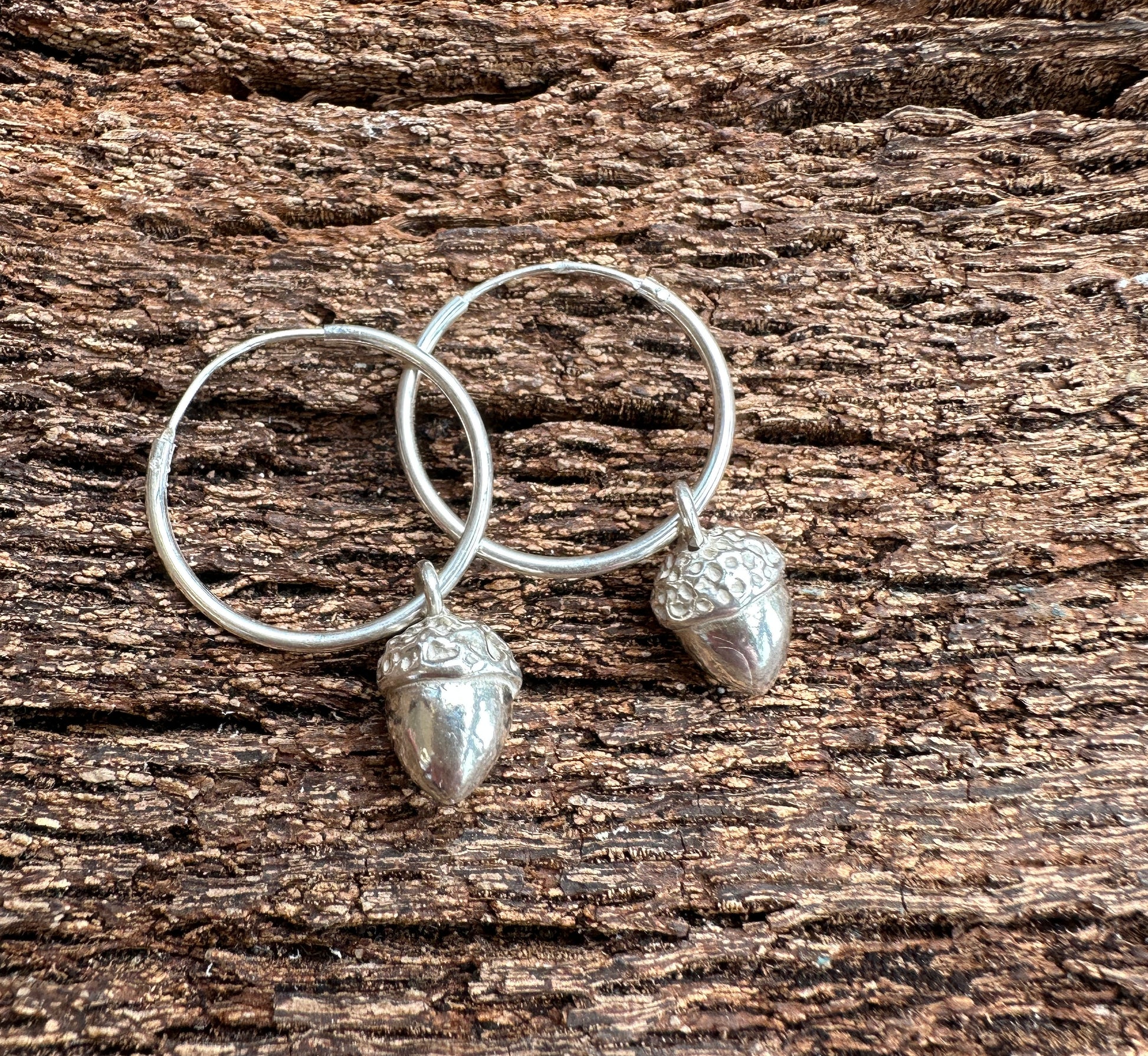 silver acorn charms on silver hoops on rough wood