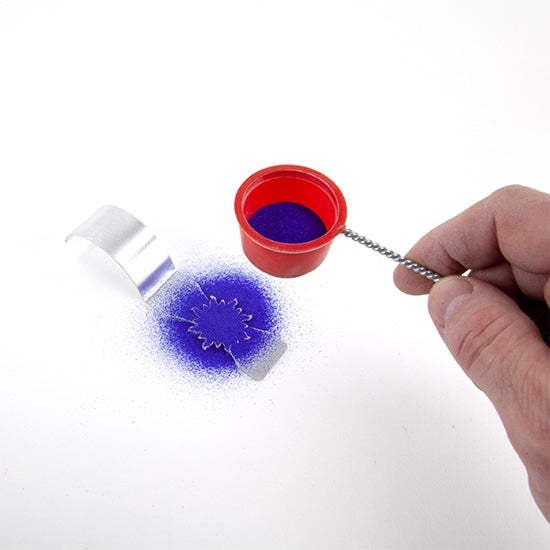 metal enameling spatula with metal blank being sifted with blue powder enamel